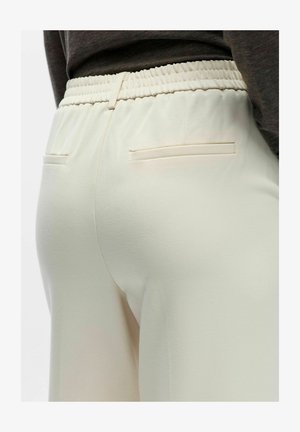 Šviesiai smėlio spalvos tamprios juosmens kelnės su lygiu paviršiumi, turinčios dvi atlošias kišenes ir laisvo kirpimo.