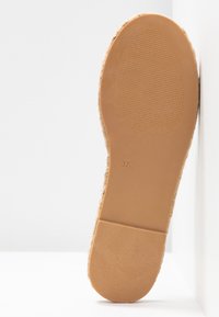 Semelle d'une chaussure taille 37 couleur beige avec des zones texturées au talon et à l'orteil, positionnée verticalement contre un fond d'angle blanc.