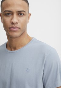 Lys blå crew-neck t-skjorte laget av myk bomull med korte ermer. Har et lite, brodert logo på venstre brystområde.