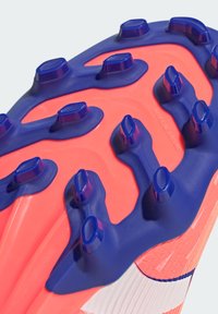Sole di scarpette da calcio con gomma rosa brillante, dotata di tacchetti blu moldati e sezioni testurizzate per una migliore presa. Inciso sulla superficie "Terreno artificiale".