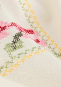 Tissu en coton avec un motif brodé multicolore aux accents rose, vert, jaune et marron. Texture lisse, drapé doux.