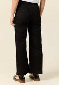 Mustat leveälahkeiset housut, joissa on korkea vyötärö, kaksi takataskua ja hieman teksturoitu kangas. Yhdistetty kiiltäviin mustiin kenkiin, joissa on pyöreä nenä.