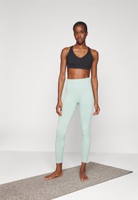 Reggiseno sportivo nero, abbinato a leggings a coste verde menta chiaro. L'outfit presenta un design aderente e una vita alta.