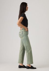 Ανοιχτό πράσινο τζιν με ίσια γραμμή και ψηλή μέση, με λεπτομέρεια ραφής σε σχήμα V στις πίσω τσέπες και δερμάτινο λογότυπο μάρκας.