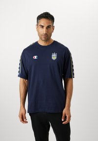 T-shirt à manches courtes marine en coton, avec un logo et trois étoiles. Rayures latérales en couleurs contrastées, col rond, coupe décontractée.