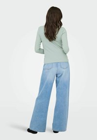 Jasnozielony top z długim rękawem i szerokie jasnoniebieskie dżinsy o luźnym kroju. Miękka tkanina z minimalną ilością detali i kieszeni.
