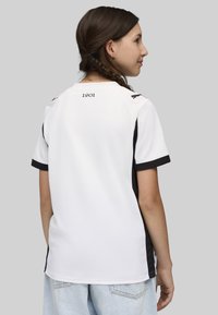 Camiseta deportiva blanca con acentos negros, mangas cortas y cuello redondo. Presenta una impresión sutil de "1901" en la parte trasera y un tejido texturizado.