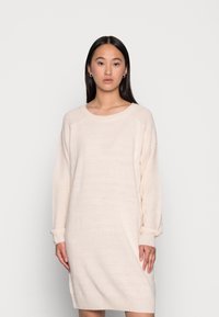 Abito lavorato a maglia beige chiaro con maniche lunghe, vestibilità rilassata, scollatura a girocollo e dettagli a costine sulle spalle e sui polsini. Texture morbida.