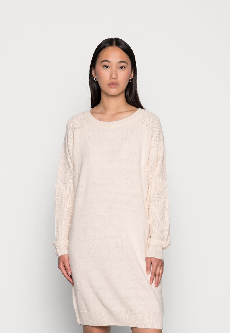 Abito lavorato a maglia beige chiaro con maniche lunghe, vestibilità rilassata, scollatura a girocollo e dettagli a costine sulle spalle e sui polsini. Texture morbida.