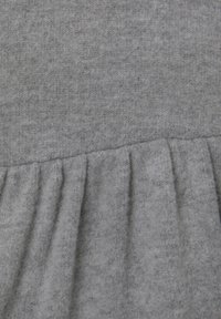 Měkká šedá pletenina s nařaseným švem, který vytváří volánkovou Texturu v dolní části.