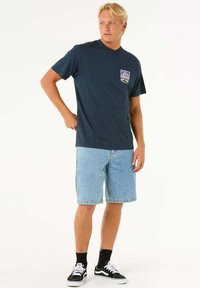 Navy cotton t-shirt with logo on chest, light blue denim shorts, and black Vans sneakers with white accents on a plain background.