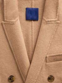Blazer en mélange de laine couleur tan avec revers en pointe, une poche poitrine unique et deux boutons marron. Comprend une étiquette bleue GAP Studio.