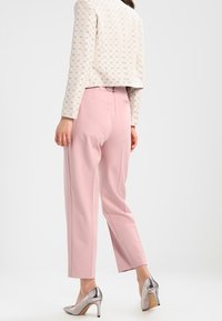 Světle růžové kalhoty na míru s volným střihem, kombinované s vzorovanou, lehkou krémovou bundou a stříbrnými lodičkami na vysokém podpatku.