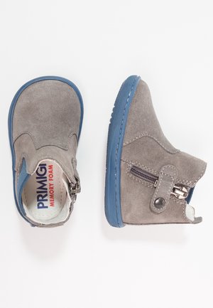 Bottines pour enfants en daim gris avec semelles en caoutchouc bleu et fermetures éclair latérales, une botte montrée de dessus et l’autre de côté.