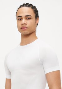 White fitted short-sleeve athletic shirt made of breathable material with textured accents on the chest and smooth sleeves.