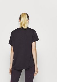 Černé tričko s krátkým rukávem, volného střihu, vyrobené z měkkého materiálu; disponuje zakulaceným lemem a bočními rozparky pro větší pohodlí.