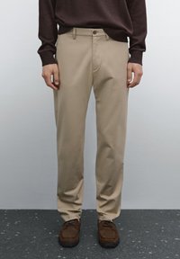 Beige trousers made of smooth fabric with a straight-leg design, featuring a front button closure and side pockets. Paired with brown shoes.