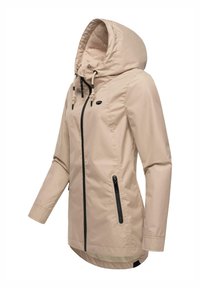 Beige waterproof jacket with a drawstring hood, black zipper accents, and a longer back hem. Smooth fabric with side pockets.