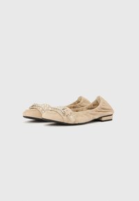 Μπεζ πάνινα παπούτσια με χαμηλή σόλα και ελαφρώς μυτερή μύτη, με ρυτιδωτή υφή, διακοσμημένα με διακοσμητικό λουράκι με στολίδια. Χαμηλό τακούνι.