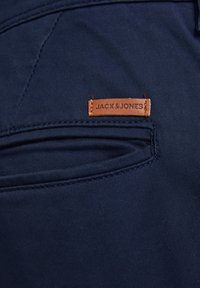 Tessuto blu navy dei pantaloni con una sottile texture. Caratterizzato da una tasca cucita e un'etichetta in pelle marrone con la scritta "JACK&JONES" in rilievo.