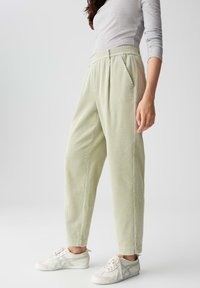 Pantaloni in corduroy verde chiaro con finitura testurizzata, dotati di vita aderente, gambe affusolate e tasche laterali, abbinati a sneakers bianche.