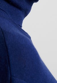 Marineblauer Rollkragenpullover aus einem weichen, strukturierten Stoff. Verfügt über einen enganliegenden Kragen und Rippendetails.