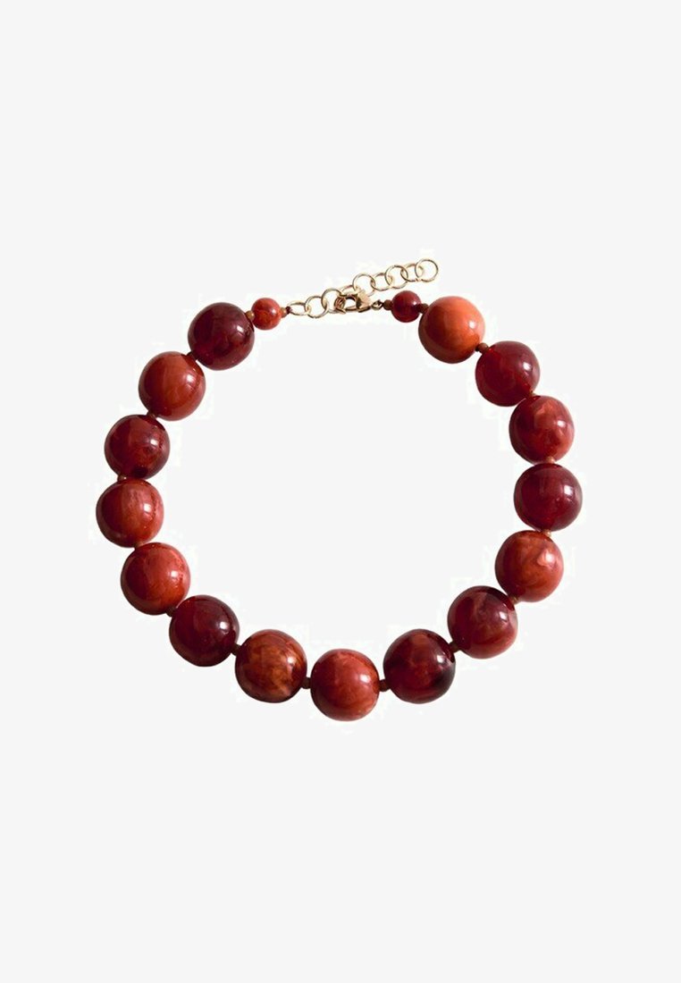 Guľaté leštené červené a hnedé korálky zavesené na náhrdelníku so zlatým nastaviteľným zapínaním na bielom pozadí.