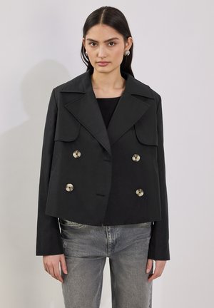 Giacca nera cropped doppiopetto con ampi rever, bottoni in tonalità argento e tasche a toppa. Il tessuto sembra liscio e strutturato.