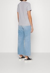 Grijze katoenen t-shirt, relaxed fit, gecombineerd met lichtblauwe wijde jeans. Zwart-witte sneakers maken de outfit compleet.