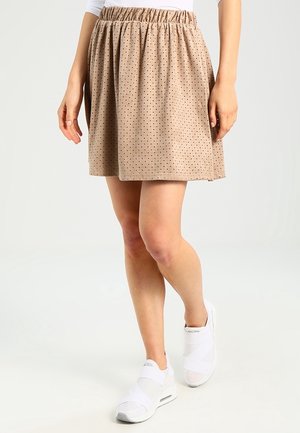 Beige nederdel med elastisk talje, med små brune prikker, letvægtsstof og en flagrende form. Sammen med hvide sko.