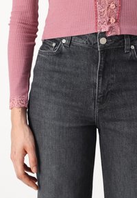 Ribana roza majica z čipkastimi poudarki na manšetah, v kombinaciji s temnimi denim hlačami. Hlače imajo srebrno kovinsko opremo in klasičen dizajn s petimi žepi.