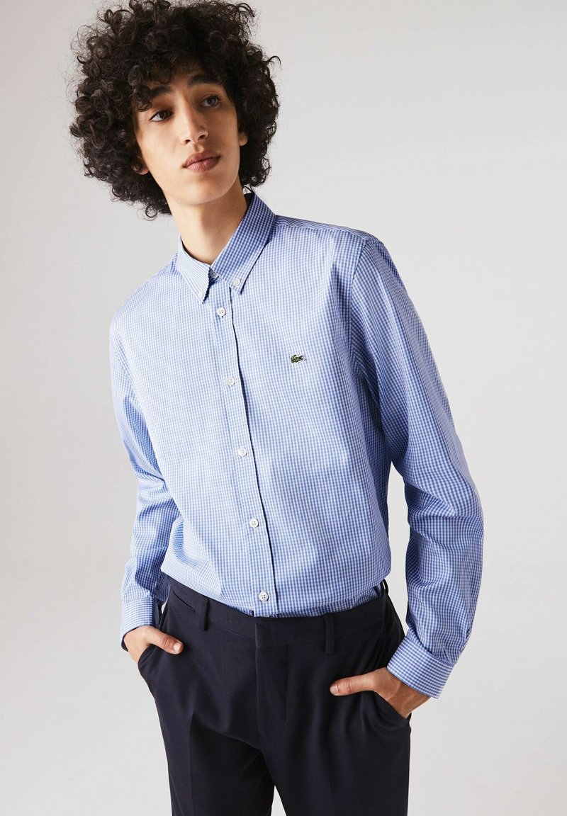 Camicia button-up a quadri blu e bianchi con colletto, caratterizzata da maniche lunghe, un design aderente e un piccolo logo verde sul petto.