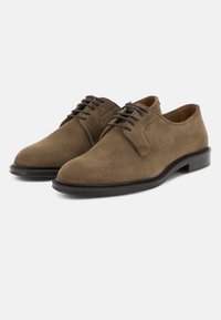 Paire de chaussures habillées en daim marron à lacets avec semelles noires sur un fond clair uni.