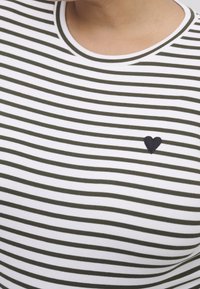 Pasyshirt w biało-oliwkowe paski, z okrągłym dekoltem i małą, czarną haftowaną serduszkiem na piersi. Gładka tekstura.