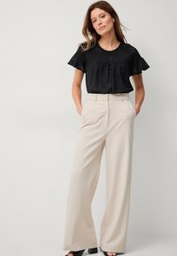 Schwarzes Spitzenoberteil mit Rü schenärmeln, kombiniert mit cremafarbigen, weiten Hosen. Das Outfit wird mit schwarzen, klobigen Sandalen mit Absatz abgerundet.