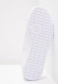 White shoe with a smooth leather upper and a textured rubber sole featuring a patterned grip and embossed logo.
