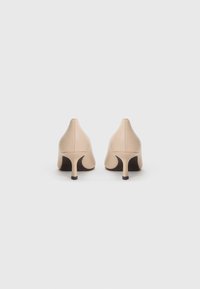 Scarpe con tacco alte in pelle color nude, caratterizzate da una punta affusolata, un design elegante e un tacco sottile con un accento scuro alla base.