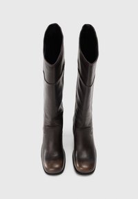 Bottes en cuir marron jusqu'au genou avec un design élégant, bout rond et une légère brillance. Texture lisse avec des détails de couture visibles.
