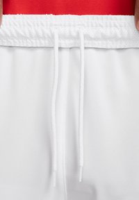 Shorts de sport blancs avec une taille à cordon et en tissu en maille, présentant une ceinture rouge unie. Texture lisse et détails de conception décontractée visibles.