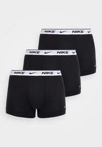 Tres calzoncillos bóxer negros de Nike con cinturas blancas que presentan logos y swooshes negros de Nike, dispuestos en una fila escalonada sobre un fondo blanco.
