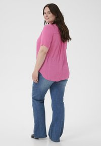 Blouse rose à manches courtes avec une finition texturée, associée à un jean bleu évasé. La tenue présente une coupe décontractée et un ourlet arrondi.