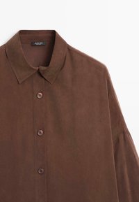 Camicia marrone con colletto, realizzata in un tessuto morbido. Presenta quattro bottoni abbinati e una vestibilità comoda.