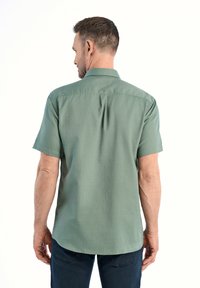Camicia a maniche corte con colletto in tessuto verde tenue, caratterizzata da una texture liscia, con yoke posteriore e dettaglio di piega.