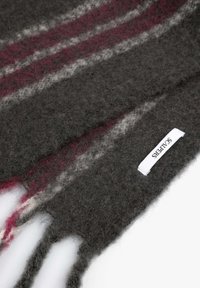 Bufanda de lana gris con rayas en burdeos y blancas. Presenta una textura suave y extremos con flecos. Incluye una etiqueta blanca con la marca "Scarlets".