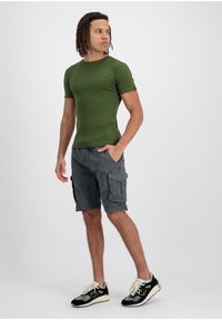 Zöld bordázott, rövid ujjú póló, amelyet szürke cargo sorttal párosítottak, oldalzsebekkel. Fekete-fehér sportcipők teszik teljessé az öltözetet.