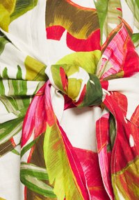 Blumenstoff in einer Mischung aus Rot, Pink, Grün und Beige, mit einem gebundenen Knoten-Detail und Blattmustern auf einem leichten Material.
