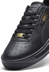 Czarne skórzane sneakersy z perforowanym noskiem, teksturowanym wykończeniem, sznurowanym designem oraz złotymi akcentami, z płaską gumową podeszwą.