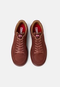Sneakers in pelle marrone con design a profilo basso, punta tonda, lacci piatti e solette rosse a contrasto. Presentano uno stile minimalista.