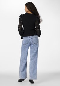 Top nero con maniche a pizzo gonfiato e texture, abbinato a jeans ampi blu chiaro e scarpe con tacco nere. Orlo arricciato sulla parte superiore.