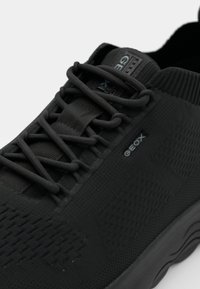 Black athletic shoe featuring a textured upper, elastic laces, and Geox branding. Rounded toe and cushioned sole for comfort.
